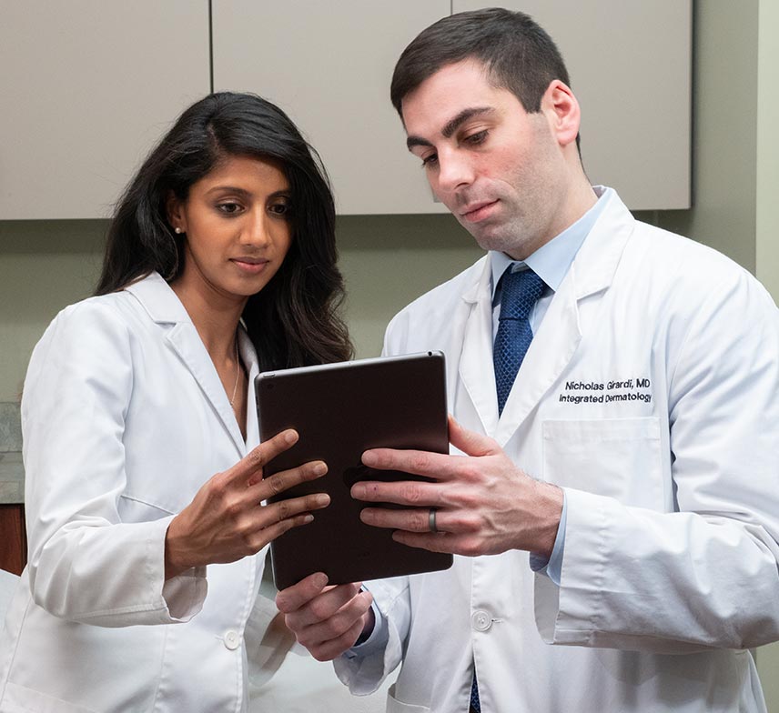 a male and female dermatologist review patient data on a tablet together