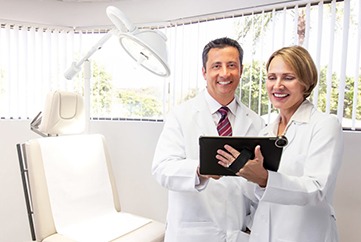 two dermatologists smiling while reviewing patient data on a tablet in an exam room